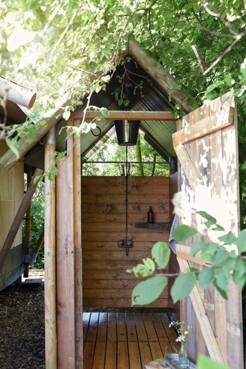 Douche extérieure à Smûk Tent Huske, Smûk Recreatie aux Pays-Bas, entourée d’arbres et de verdure.