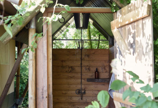 Douche extérieure à Smûk Tent Huske, Smûk Recreatie aux Pays-Bas, entourée d’arbres et de verdure.