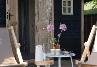 Coin salon extérieur rustique avec chaises, tables et fleurs au Smûk Tent Huske, Smûk Recreatie, Pays-Bas.