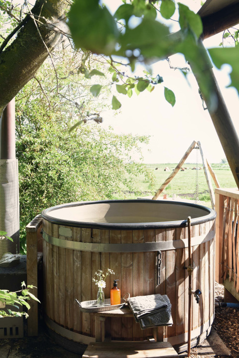 Bain à remous en bois en plein air à côté d’une tente safari à Smûk Recreatie aux Pays-Bas, entouré de verdure.