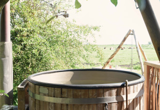 Bain à remous en bois en plein air à côté d’une tente safari à Smûk Recreatie aux Pays-Bas, entouré de verdure.