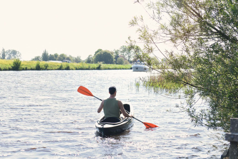 Persoon in een kajak op de rivier bij Smûk Tent Huske, Smûk Recreatie, Nederland, omgeven door natuur.