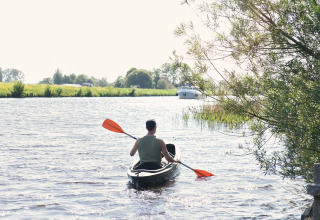 Persoon in een kajak op de rivier bij Smûk Tent Huske, Smûk Recreatie, Nederland, omgeven door natuur.