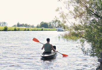 Persoon in een kajak op de rivier bij Smûk Tent Huske, Smûk Recreatie, Nederland, omgeven door natuur.