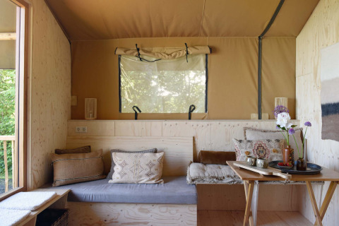 Knus zitgedeelte in Smûk Tent Huske met kussens, houten accenten en licht bij Smûk Recreatie, Nederland.