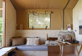 Knus zitgedeelte in Smûk Tent Huske met kussens, houten accenten en licht bij Smûk Recreatie, Nederland.