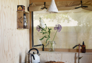 Petite cuisine rétro sous tente safari avec pain, œufs, bouilloire, vase de fleurs et réfrigérateur.