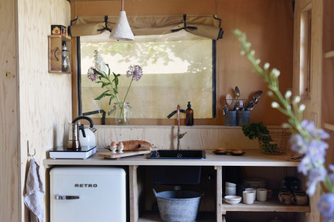 Cuisine de tente safari avec frigo rétro, bois clair et fleurs en vase à Smûk Recreatie aux Pays-Bas.