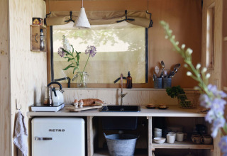 Cuisine de tente safari avec frigo rétro, bois clair et fleurs en vase à Smûk Recreatie aux Pays-Bas.