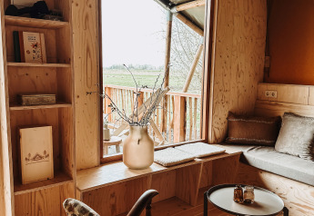 Gezellige inrichting in Smûk Tent Huske bij Smûk Recreatie met houten meubels en groot raam met uitzicht.