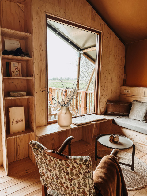 Intérieur chaleureux du safari-tente Smûk Tent Huske aux Pays-Bas avec mobilier en bois et grande fenêtre.