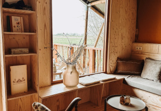 Intérieur chaleureux du safari-tente Smûk Tent Huske aux Pays-Bas avec mobilier en bois et grande fenêtre.