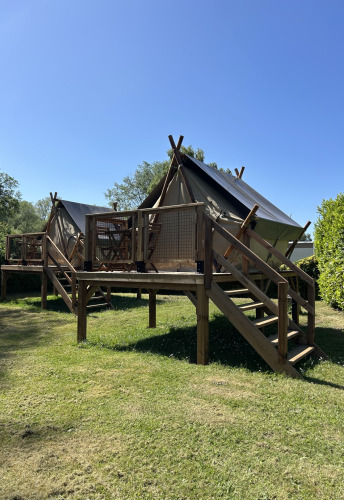 Tienda safari SLOW LIFE VERBLIJF sobre una plataforma de madera, rodeada de césped y cielo azul.