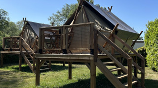 Tienda safari SLOW LIFE VERBLIJF sobre una plataforma de madera, rodeada de césped y cielo azul.