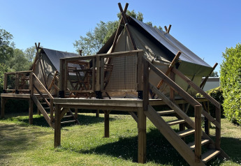 Tienda safari SLOW LIFE VERBLIJF sobre una plataforma de madera, rodeada de césped y cielo azul.