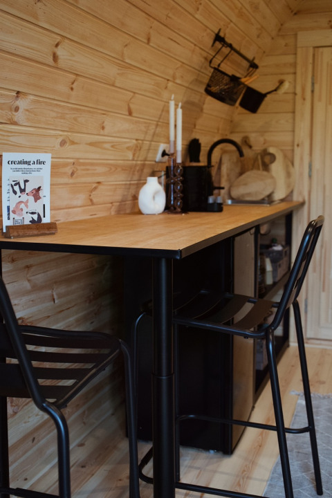 Interno di pod glamping moderno con pareti in legno, tavolo bar e sedie nere da REBL Outdoor nei Paesi Bassi.