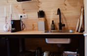 Petite cuisine en bois avec évier noir, ustensiles et étagères ouvertes dans une glamping pod aux Pays-Bas.