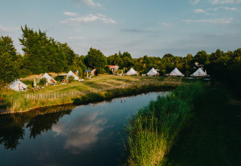 Area glamping con tende, lago, prato verde e sauna presso REBL Outdoor nei Paesi Bassi.