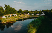 Site de glamping avec tentes, étang, pelouse verte et sauna chez REBL Outdoor aux Pays-Bas.
