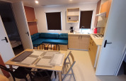 Moderno cottage con cucina, tavolo da pranzo, divano blu e due camere al Camping Floreal La Roche-en-Ardenne.