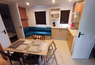 Moderno cottage con cucina, tavolo da pranzo, divano blu e due camere al Camping Floreal La Roche-en-Ardenne.