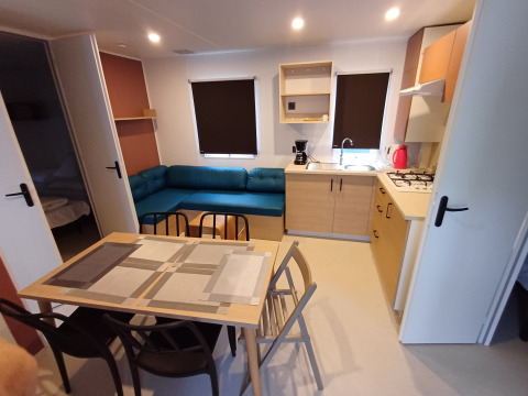 Moderno cottage con cucina, tavolo da pranzo, divano blu e due camere al Camping Floreal La Roche-en-Ardenne.