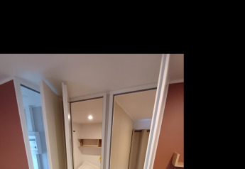 Innenansicht eines Cottages auf Camping Floreal La Roche-en-Ardenne mit Bett, Sofa und moderner Einrichtung.