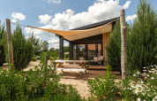 Casa diminuta Sand Lodge con terraza y toldo en Holiday Park De IJsvogel, rodeada de vegetación.