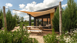 Tiny house Sand Lodge met terras en schaduwdoek bij Holiday Park De IJsvogel, omringd door natuur.