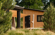 Sand Lodge Tiny House im Ferienpark De IJsvogel in den Niederlanden, umgeben von Bäumen und Sträuchern.