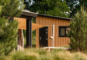 Casa diminuta Sand Lodge en Holiday Park De IJsvogel, Países Bajos, rodeada de árboles y vegetación.