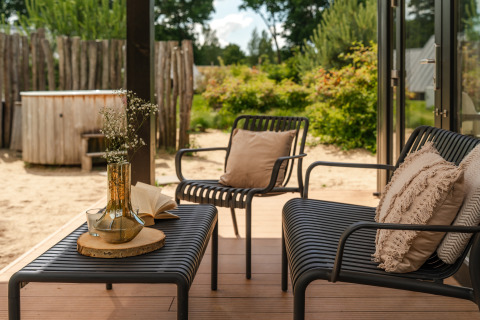 Udendørs siddeområde med sorte stole, beige puder, bord med vase og jacuzzi i baggrunden ved Sand Lodge.