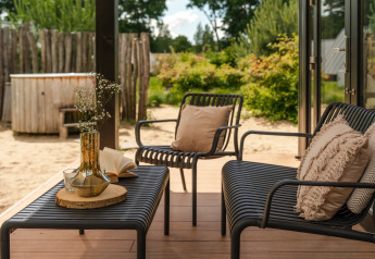 Outdoor lounge area with black chairs, beige pillows, and a hot tub at Sand Lodge Jacuzzi, De IJsvogel.