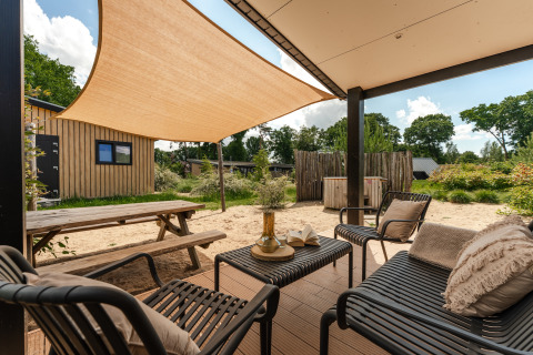 Terras met zitjes bij Sand Lodge Jacuzzi, Holiday Park De IJsvogel, Nederland, met schaduwdoek en tuin.