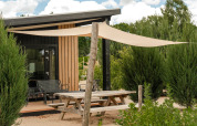 Mesa de picnic exterior y toldo frente a la tiny house Sand Lodge Sauna en Holiday Park De IJsvogel, Países Bajos.