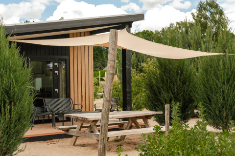 Tavolo da picnic all'aperto e vela ombreggiante davanti alla tiny house Sand Lodge Sauna a Holiday Park De IJsvogel, Paesi Bassi.