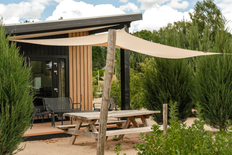 Picknicktafel en schaduwdoek bij de tiny house Sand Lodge Sauna in vakantiepark De IJsvogel, Nederland.