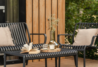 Gezellige zithoek buiten bij Sand Lodge Sauna, Holiday Park De IJsvogel, met zwarte stoelen en tafel.