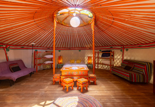 Interior de una yurta tradicional con muebles pintados coloridos, vigas de madera y áreas de descanso.