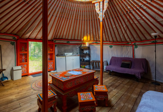 Vista interior de una yurta tradicional con muebles coloridos, suelo de madera y una pequeña zona de cocina.