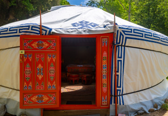 Yurt med farverig dekoreret dør og traditionelle motiver ved Camping Des Randonneurs i Frankrig, omkranset af skov.