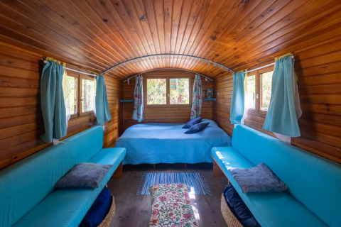 Interior de la Gipsy wagon en Camping Des Randonneurs, Francia, con paredes de madera y sofás azules.