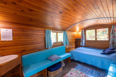 Vista interior de una cabaña de madera con sofá azul y cama en Camping Des Randonneurs, Francia.