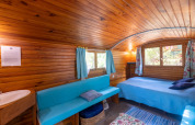 Indvendig udsigt af en træhytte med blå sofa, seng og vinduer, på Camping Des Randonneurs i Frankrig.