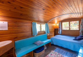Vista interior de una cabaña de madera con sofá azul y cama en Camping Des Randonneurs, Francia.