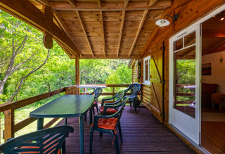 Porche de madera con mesa y sillas en el Chalet del Camping Des Randonneurs, rodeado de árboles verdes.