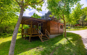 Træchalet med veranda midt i naturen på Camping Des Randonneurs i Frankrig, omgivet af grønne træer.