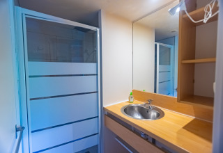 Baño con encimera de madera, lavabo redondo, gran espejo y ducha en Chalet de Camping Des Randonneurs, Francia.