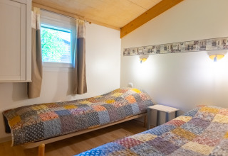 Dormitorio con dos camas individuales, colchas patchwork y detalles de madera en Chalet Camping Des Randonneurs, Francia.