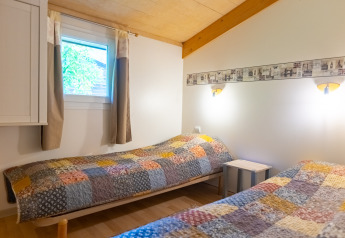 Soveværelse med to enkeltsenge, lappetæpper og lyse trædetaljer i Chalet på Camping Des Randonneurs, Frankrig.